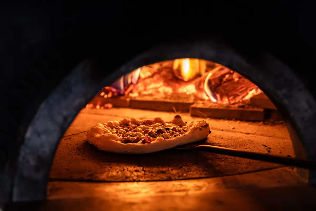 A pizza on a peel going into the glowing brick oven