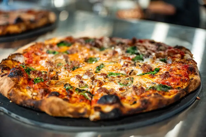 A brick oven pizza fresh out of the oven with charred crust