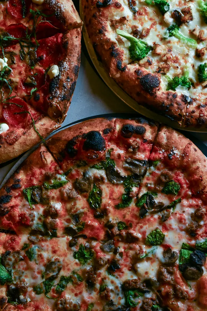 Three brick oven pizzas with blistered crust, fresh from the oven